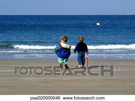 Stock Photograph - Children standing on beach, rear view. Fotosearch