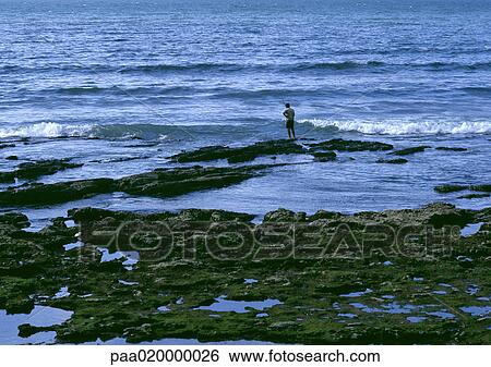 Stock Photograph - Person standing on rock near breaking waves. Fotosearch