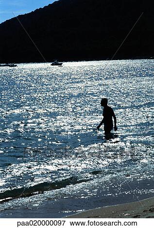 Stock Photo - Person wading in sea, mountain in background. Fotosearch