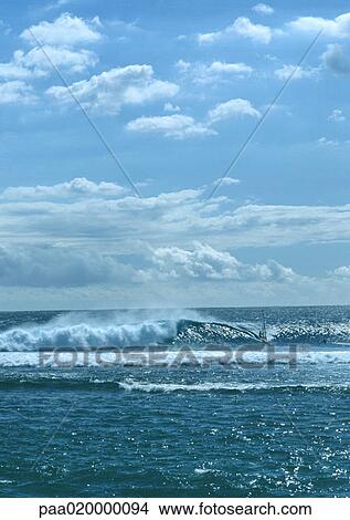 Picture - Waves crashing in ocean under blue sky with clouds. Fotosearch