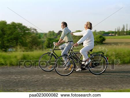 Couple riding bicycles together in countryside View Large Photo Image Stock Image - Couple riding bicycles together in countryside. Fotosearch