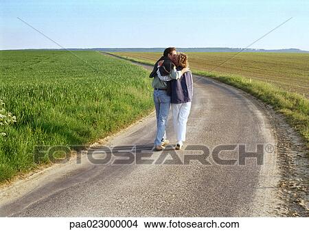 Picture - Couple walking in road in between two green fields.. Fotosearch