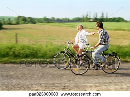 Man and woman riding bicycles, holding hands, countryside in background View Large Photo Image Stock Image - Man and woman riding bicycles, holding hands, countryside in background. Fotosearch