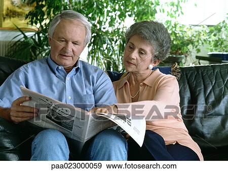 Stock Photo - Senior couple on couch reading newspaper.. Fotosearch
