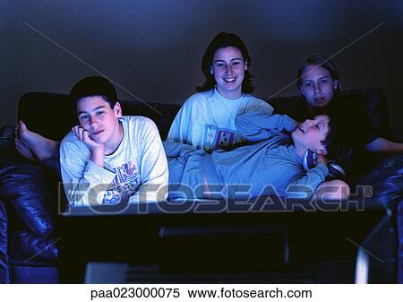 Young adults sitting together on couch watching television in the dark. View Large Photo Image Stock Photography - Young adults sitting together on couch watching television in the dark.. Fotosearch