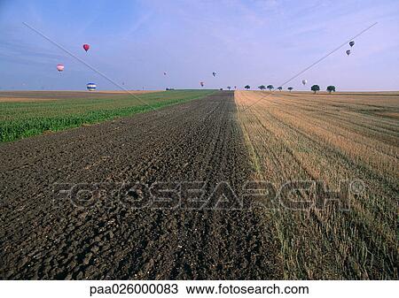 Stock Image - France, Lorraine, plowed field with hot air balloons in distance. Fotosearch