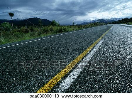 Stock Image - New Zealand, wet road, stormy weather in distance.. Fotosearch