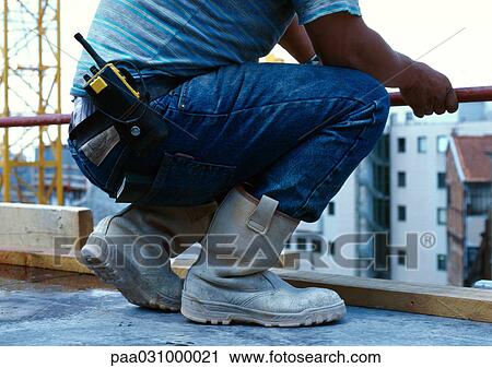 Stock Image - Man crouching on construction site, low section. Fotosearch
