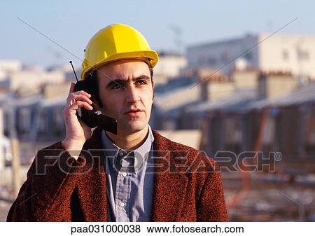 Stock Photo - Man wearing hard hat, using cell phone. Fotosearch