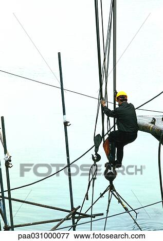 Stock Photo - Man with hard hat holding on to cables above water. Fotosearch