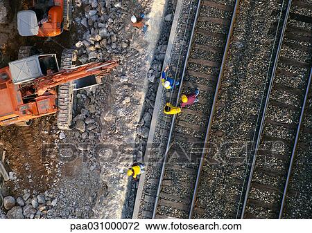 Stock Image - Men wearing hard hats, standing on rails, elevated view. Fotosearch