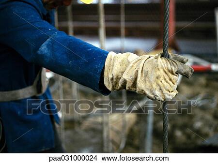 Picture - Person with gloved hand holding cable on construction site, close-up. Fotosearch