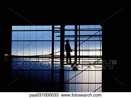 Stock Image - Silhouette of man standing on scaffolding. Fotosearch