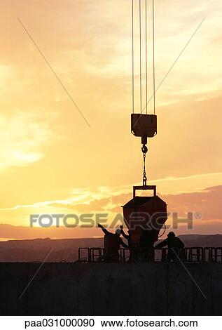 Stock Image - Silhouettes of workers near cement mixer at sunrise. Fotosearch
