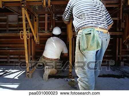 Stock Image - Two workers in construction site, rear view. Fotosearch