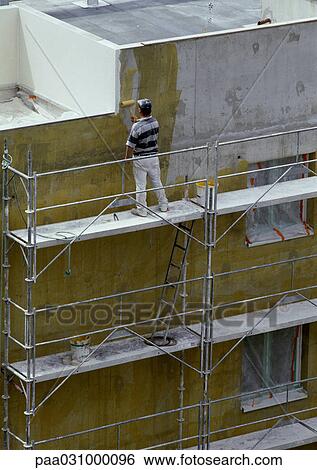 Stock Photograph - Worker on scaffolding, painting wall. Fotosearch