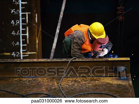Stock Photograph - Worker wearing protective mask, welding metal beam. Fotosearch