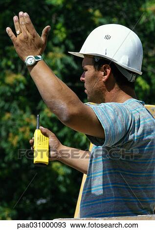 Stock Image - Worker with hard hat, holding walkie-talkie, side view. Fotosearch
