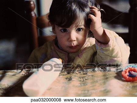 Stock Photo - Boy sitting with baby bottle on table, portrait. Fotosearch