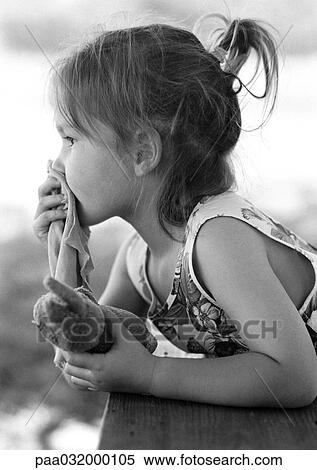 Stock Photography - Girl holding stuffed animal in hand and piece of fabric over mouth, side view, b&w. Fotosearch