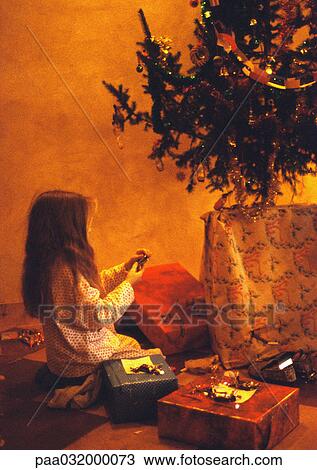 Girl kneeling in front of Christmas tree, looking at presents View Large Photo Image Stock Image - Girl kneeling in front of Christmas tree, looking at presents. Fotosearch