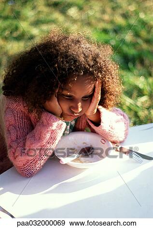 Stock Photo - Girl leaning on outdoor table, holding head. Fotosearch