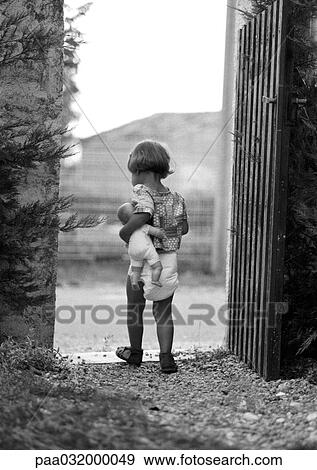 Stock Photo - Little girl holding baby doll in gateway, rear view, b&w. Fotosearch