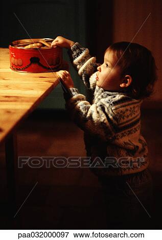 Stock Photo - Toddler reaching for cookies on table, side view. Fotosearch