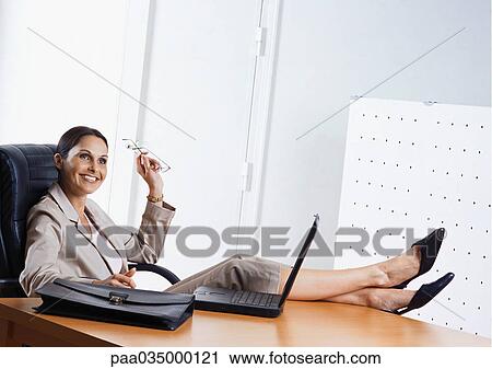 Businesswoman sitting at desk with feet on table, smiling View Large Photo Image Stock Image - Businesswoman sitting at desk with feet on table, smiling. Fotosearch
