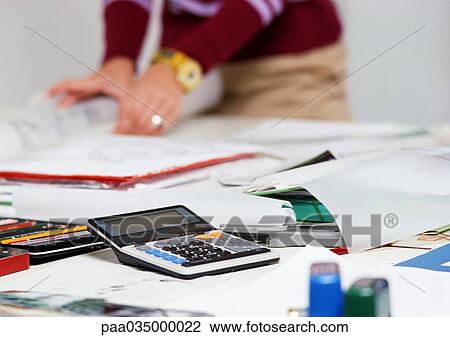 Stock Image - Caculator on desk, person in background. Fotosearch