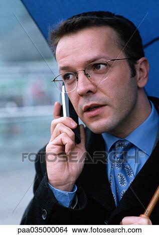 Picture - Man holding cell phone and umbrella, portrait. Fotosearch