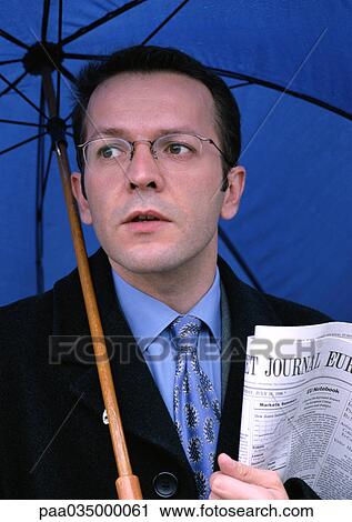 Stock Image - Man holding umbrella and newspaper, portrait. Fotosearch