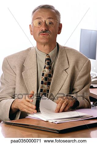 Stock Image - Man sitting at desk, holding document. Fotosearch