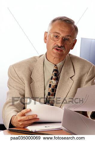 Man sitting at desk, holding document View Large Photo Image Stock Photo - Man sitting at desk, holding document. Fotosearch