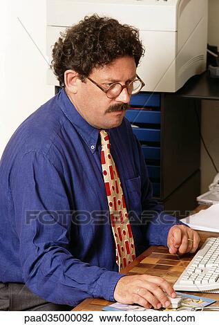 Man sitting at desk, holding mouse View Large Photo Image Stock Image - Man sitting at desk, holding mouse. Fotosearch