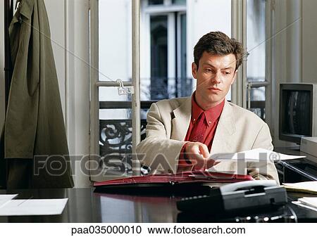 Stock Image - Man sitting at desk, holding paper. Fotosearch