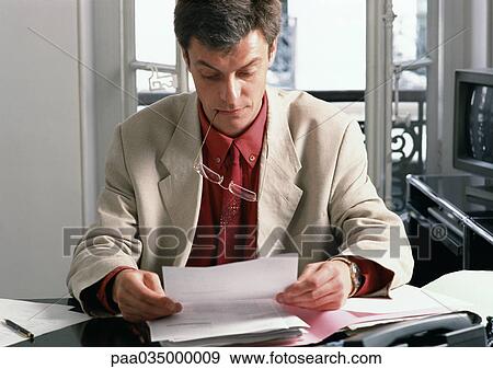 Man sitting at desk, reading document View Large Photo Image Stock Photo - Man sitting at desk, reading document. Fotosearch