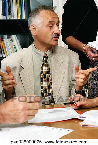 Stock Photograph - Man sitting at table, gesturing with hands. Fotosearch