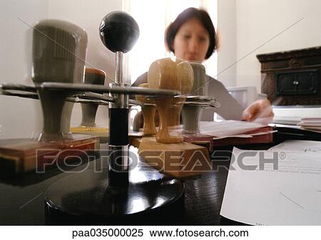 Stock Photography - Stampers on rack, and woman sitting at desk, blurred. Fotosearch