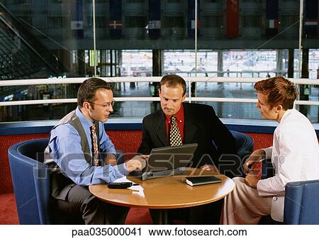 Two men and a woman sitting at table, looking at laptop computer View Large Photo Image Stock Image - Two men and a woman sitting at table, looking at laptop computer. Fotosearch