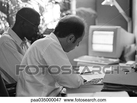 Stock Photo - Two men sitting at desk, b&w. Fotosearch