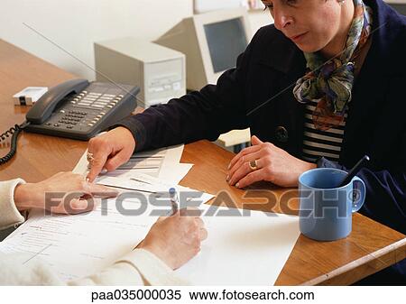 Stock Photography - Two people sitting across from each other at table, looking at document. Fotosearch