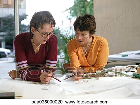 Two women leaning on table, holding pens View Large Photo Image Stock Image - Two women leaning on table, holding pens. Fotosearch