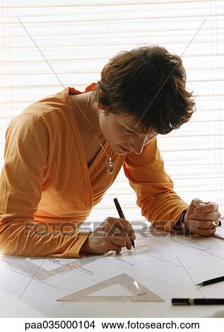 Picture - Woman bending over table, holding pen. Fotosearch