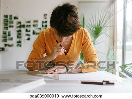 Stock Photo - Woman bending over table, holding set square and pen. Fotosearch