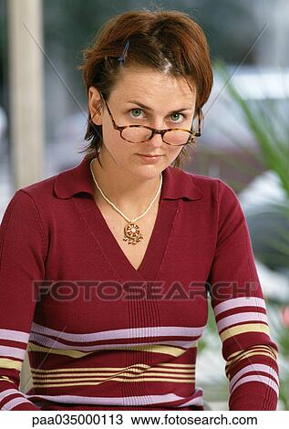 Stock Image - Woman looking over edge of glasses, portrait. Fotosearch