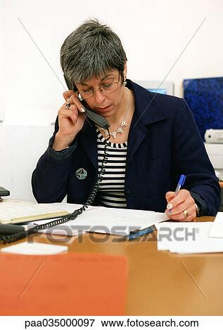 Stock Photo - Woman sitting at desk, telephoning. Fotosearch