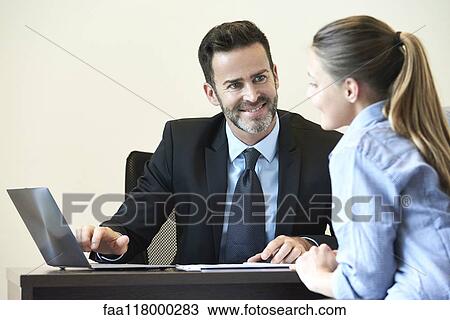 Stock Image - Businessman and businesswoman having meeting in office. Fotosearch