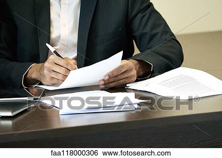 Businessman checking a document on his desk View Large Photo Image Stock Photograph - Businessman checking a document on his desk. Fotosearch