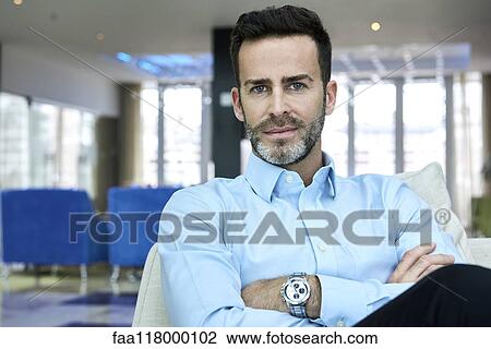Stock Image - Businessman sitting on sofa with arms crossed. Fotosearch
